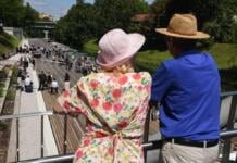 A couple of hatted tourists standing on a bridge with their backs turned to the camera.