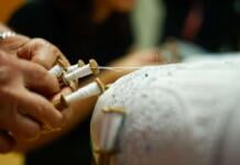 A pair of hands holding bobbins attached to a lace pillow.